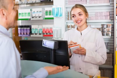 Friendly young female pharmacist serving and consulting men in pharmacy